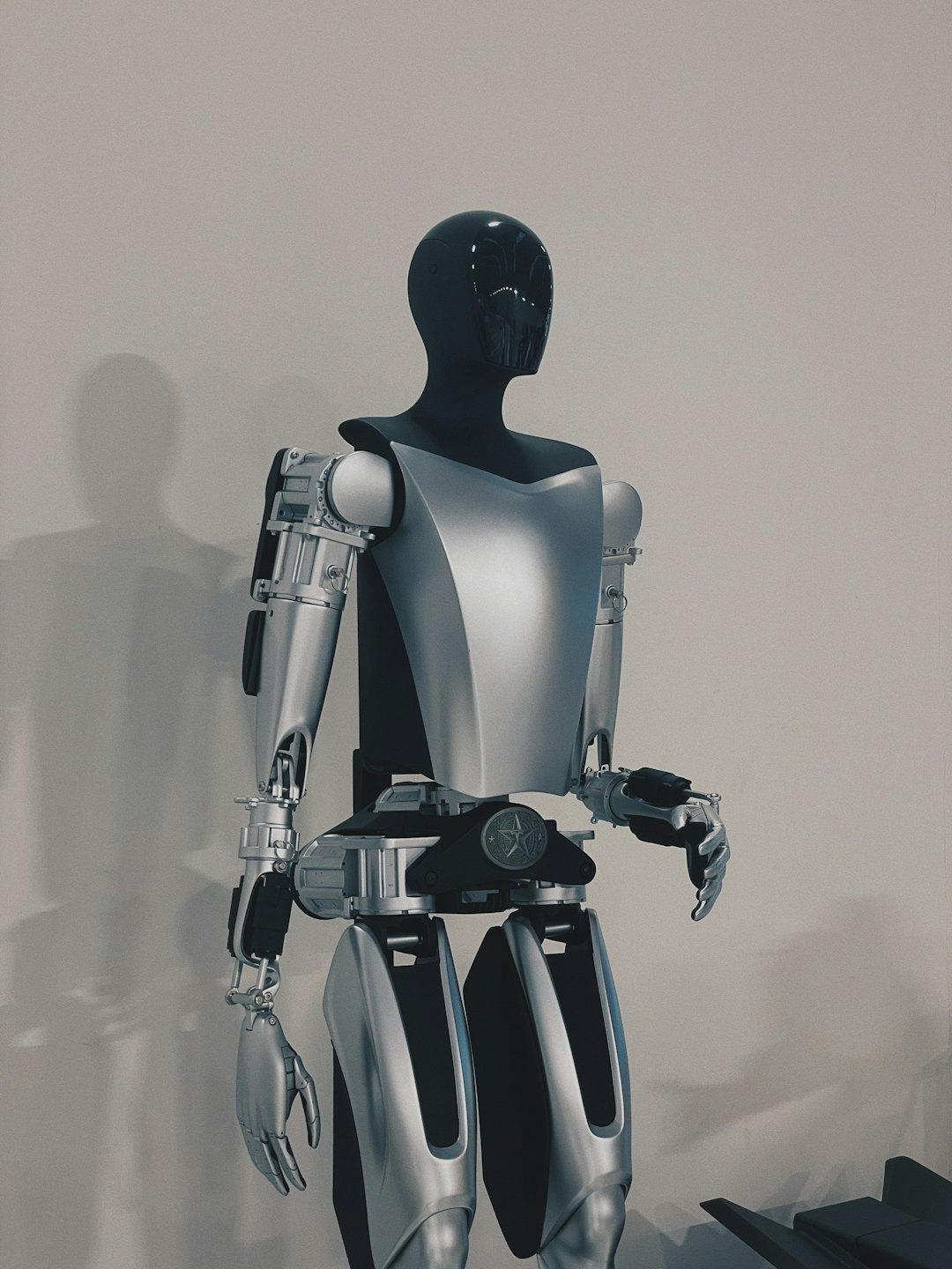 Humanoid robot standing against a light grey wall.