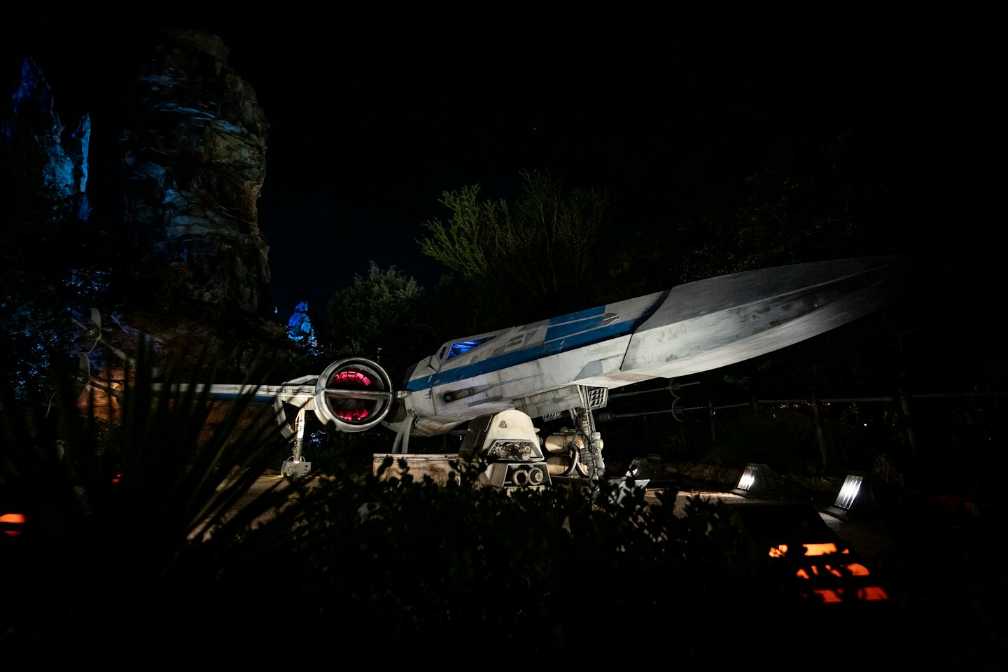 Futuristic spaceship with red engine lights on dark ground at night.