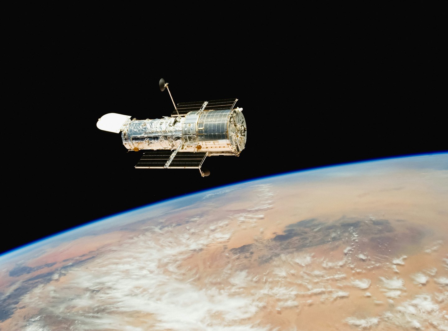 The Hubble Space Telescope orbits above Earth's blue atmosphere.