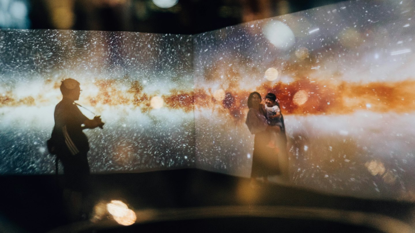 Family watches a digital galaxy projection in an indoor exhibit.